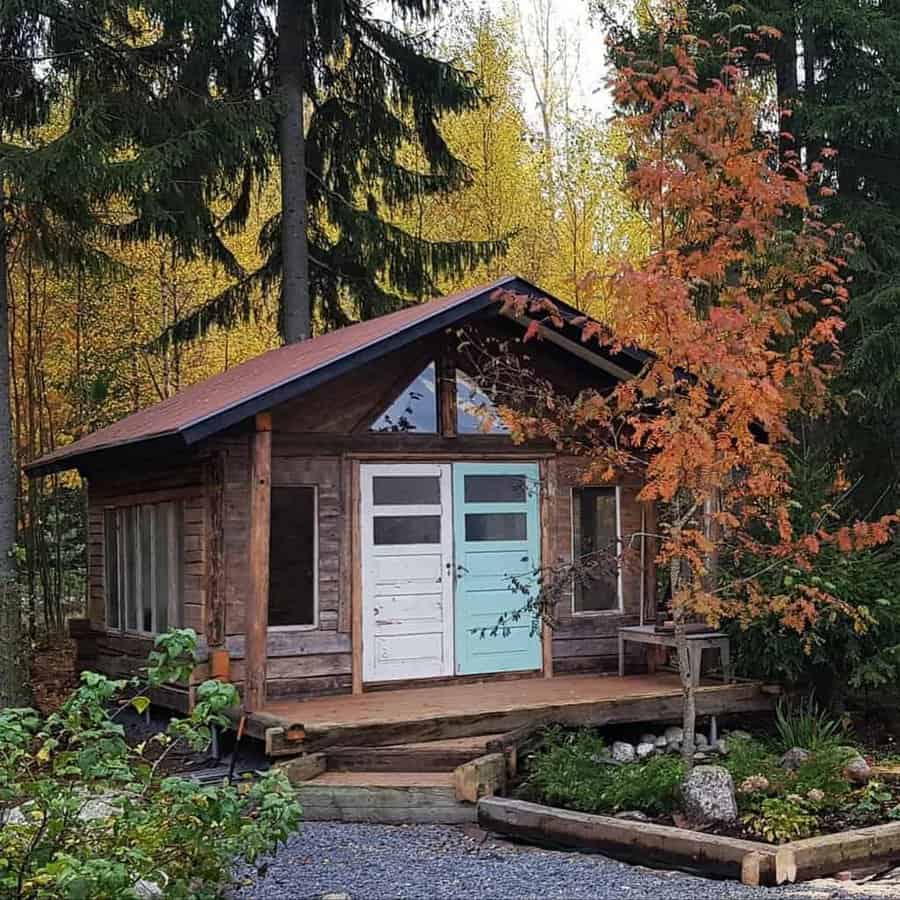 A rustic cabin with a double door and autumn foliage in a forested setting