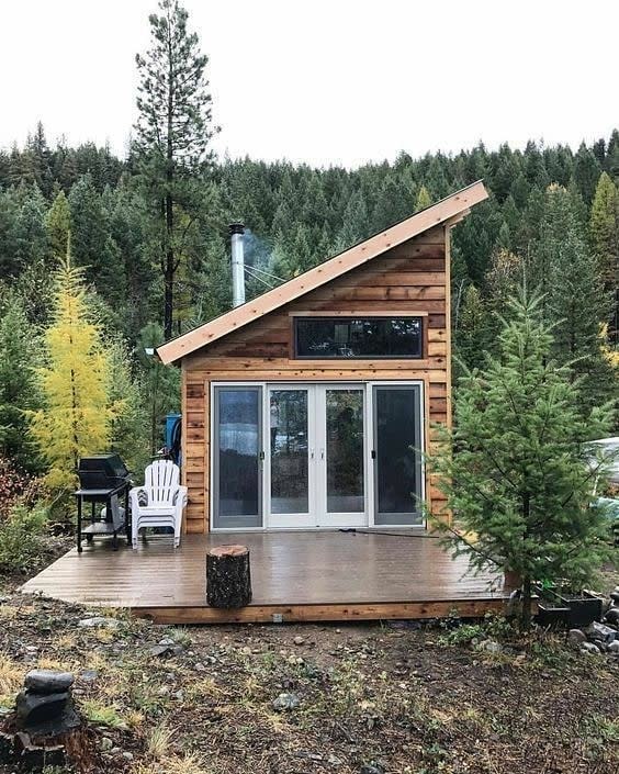 A small wooden cabin with a slanted roof surrounded by trees and forest