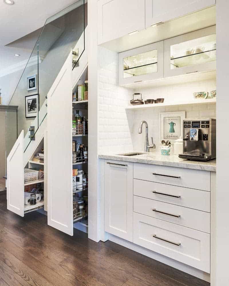 Compact kitchen under a staircase with white cabinets, a coffee maker, and a pull-out pantry