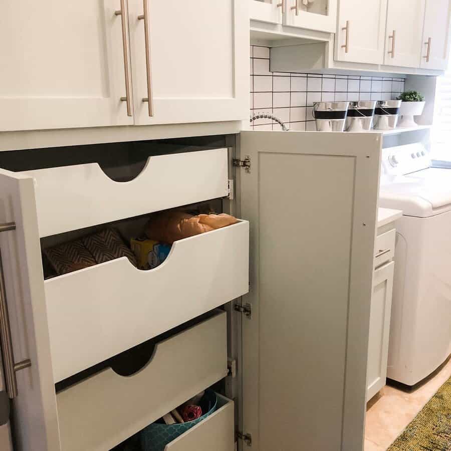 Tall kitchen cabinet with drawers open, revealing pantry storage with various items, white cabinets and a glimpse of a laundry area