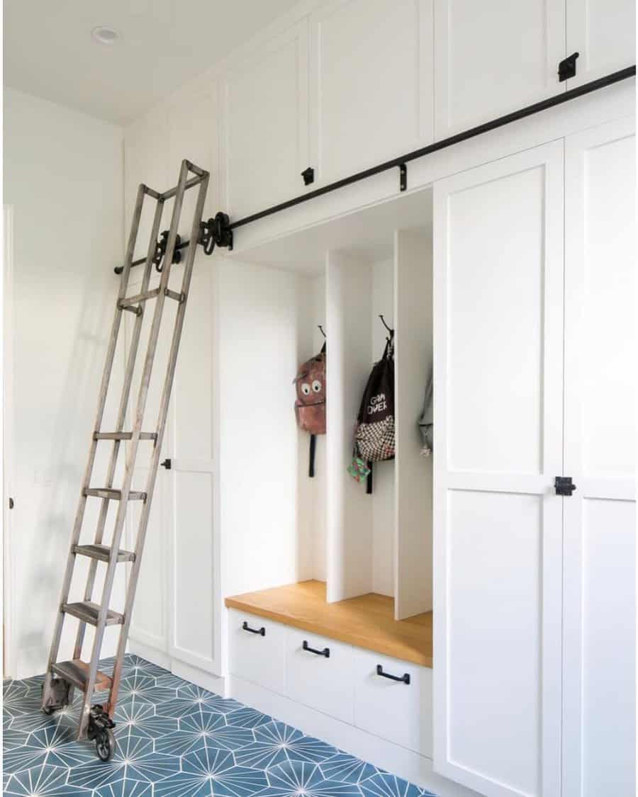 A functional mudroom with built-in white cabinets, a wooden bench, cubby storage, and a sliding ladder for easy access to upper storage