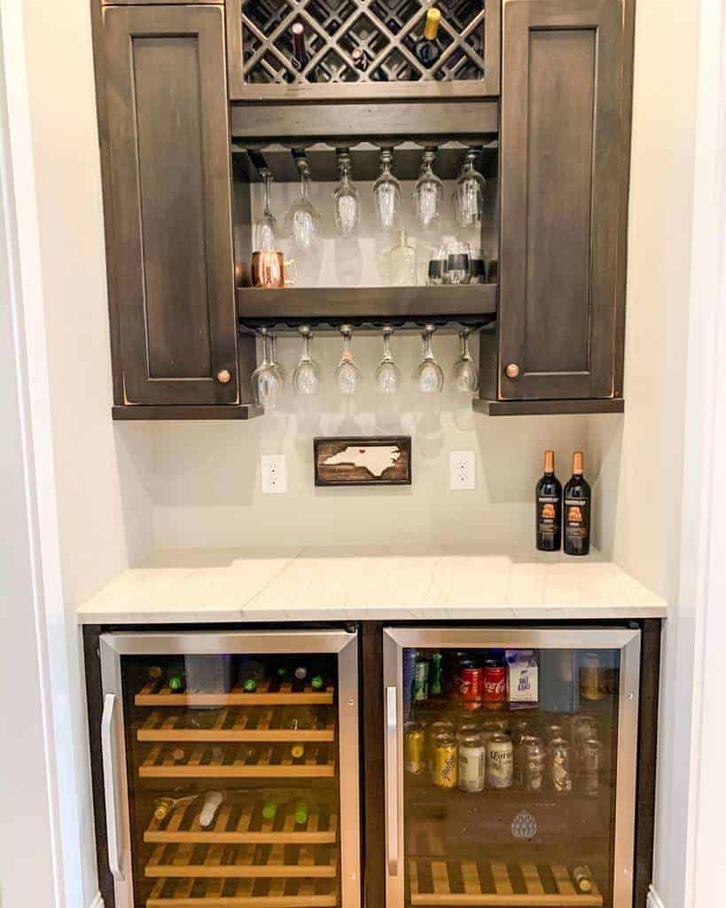 Home wine bar with a wine rack, hanging glasses, two wine coolers stocked with drinks, and a small wall decoration