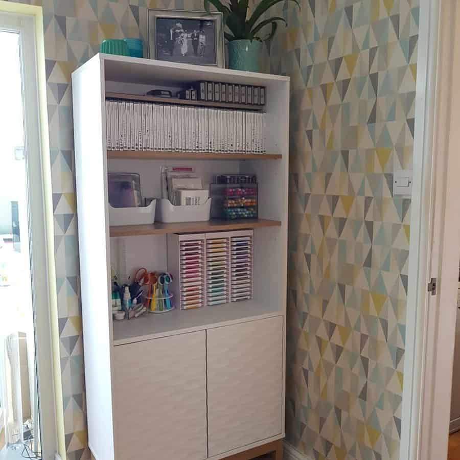 White bookcase with art supplies and patterned wallpaper