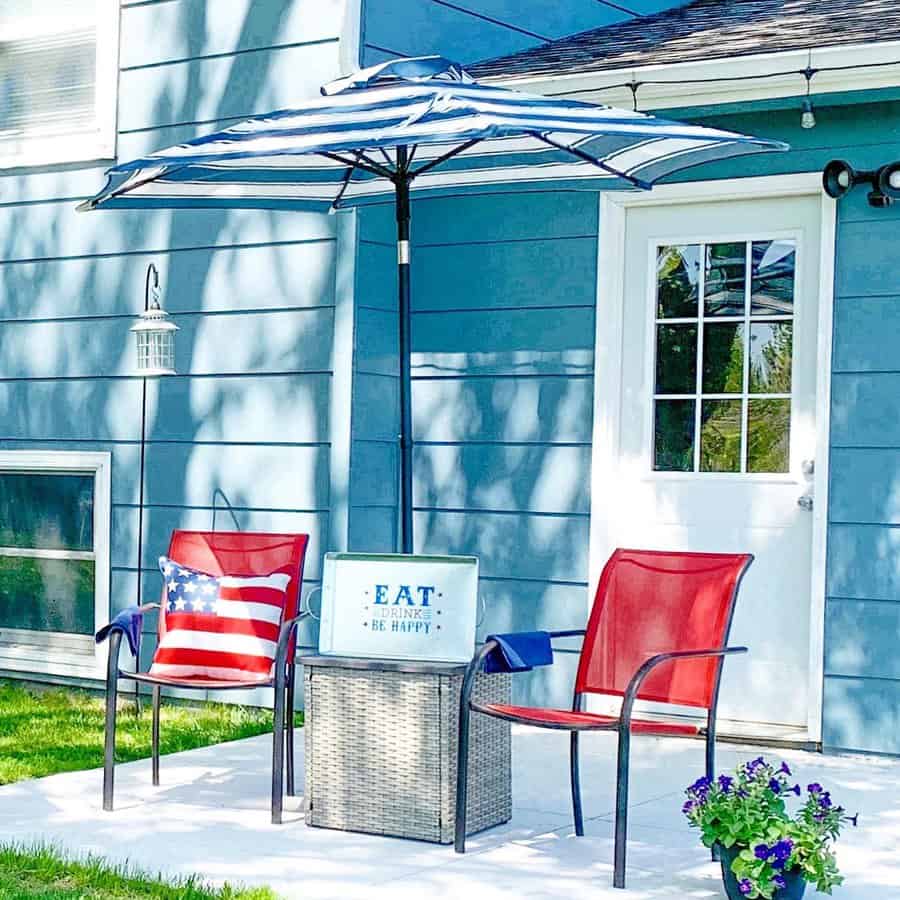 Simple backyard patio with a striped umbrella, red chairs, and a small wicker table, creating a shaded spot for relaxing outdoors