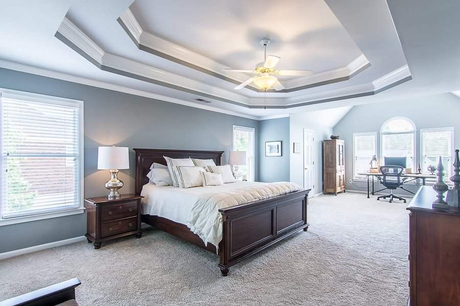 Spacious master bedroom with a tray ceiling, ceiling fan, large bed, and desk by arched windows filled with soft natural light