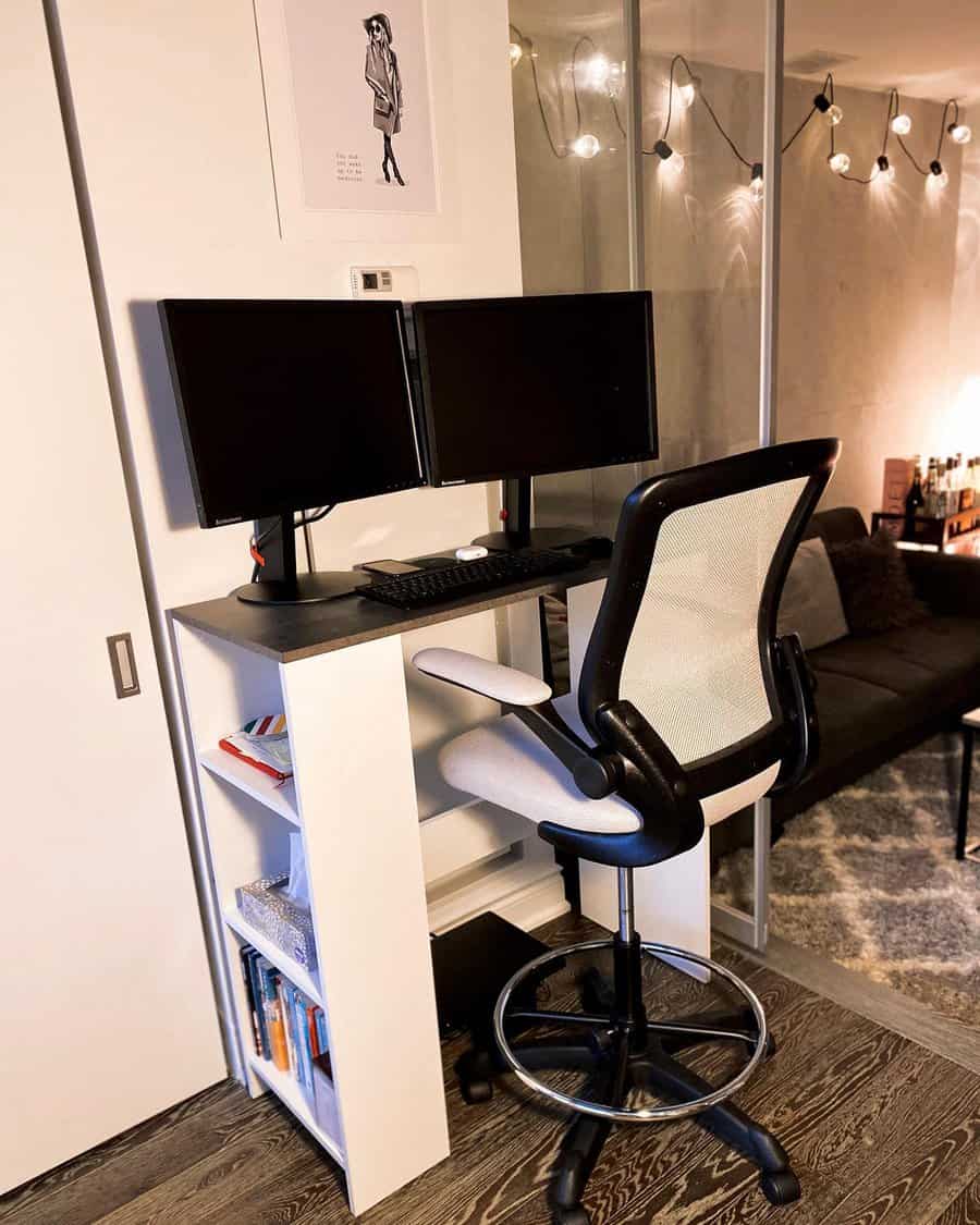 Standing desk setup with dual monitors, keyboard, and mouse; high chair and books on shelves; string lights adorn the glass wall