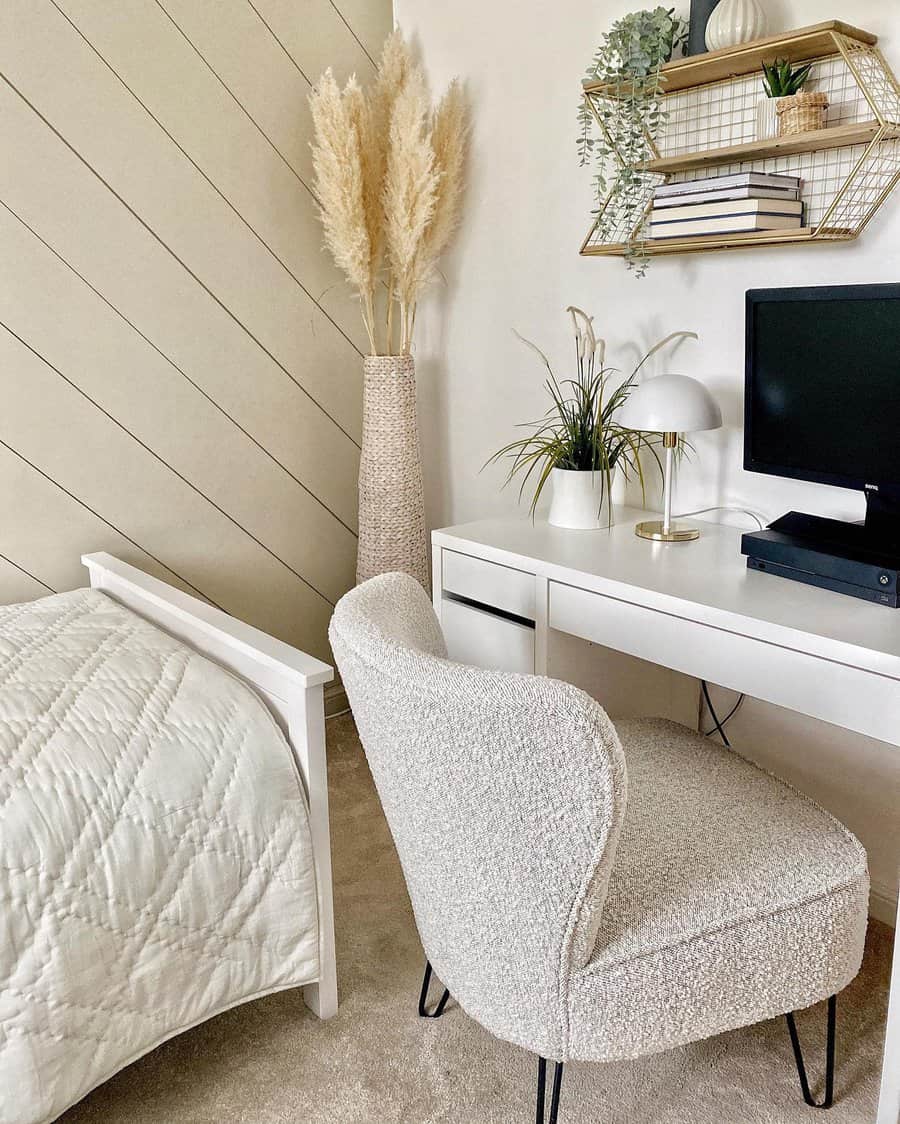 Cozy bedroom corner with a white desk, textured chair, computer, decorative plants, and pampas grass in neutral tones and modern decor