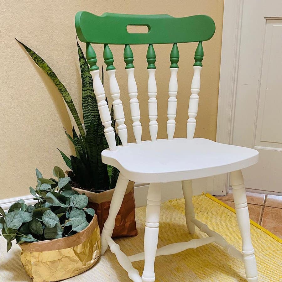 Vintage wooden chair painted white with a green accent on the top rail and spindles, styled with potted plants in a cozy corner.