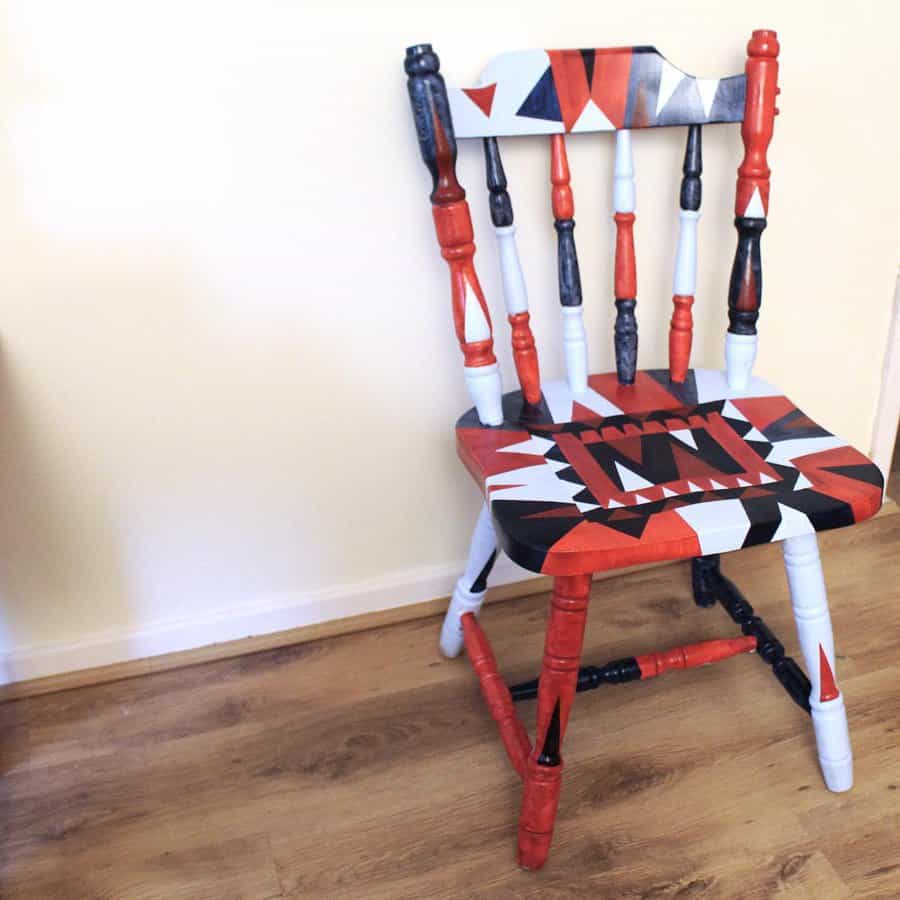 Wooden chair with a bold geometric hand-painted design in red, black, and white, featuring intricate patterns on the seat and spindles.