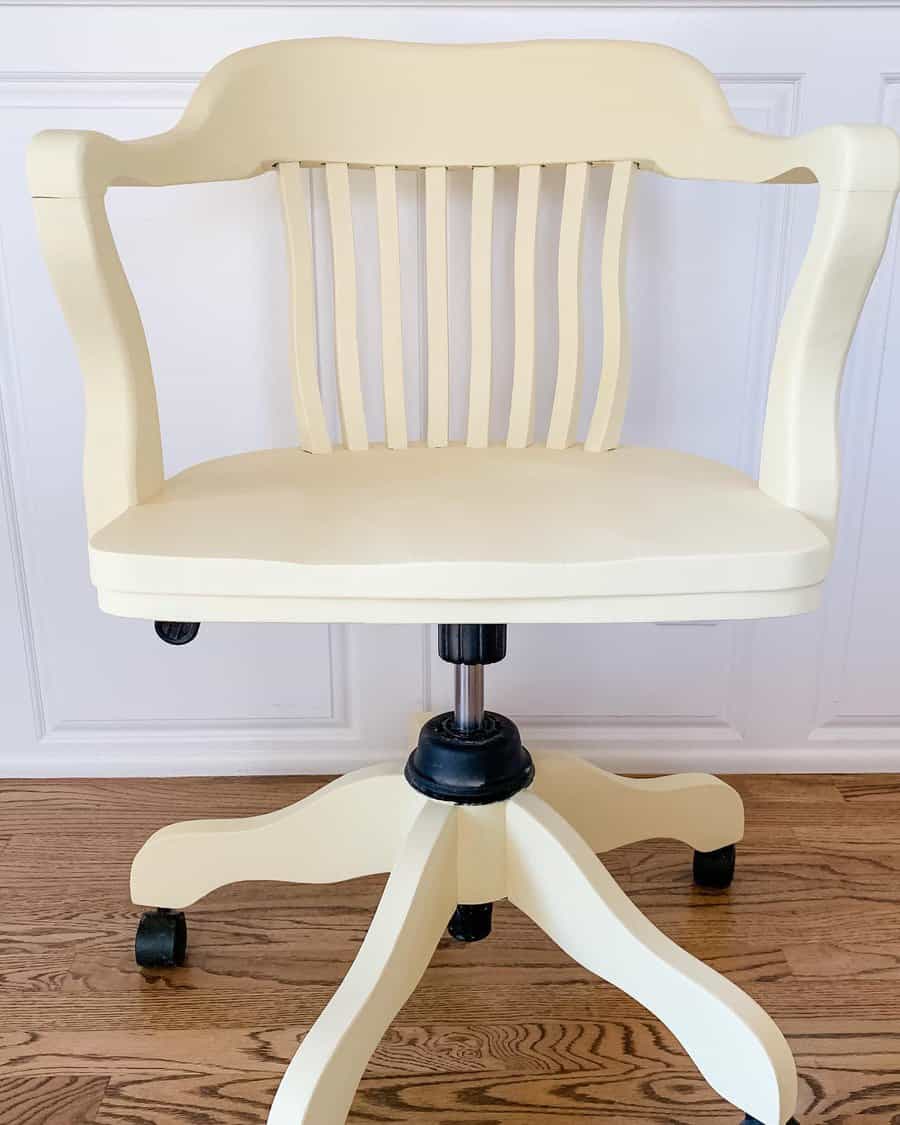 Vintage wooden swivel chair painted in soft cream, featuring curved armrests and a slatted back, set on a sturdy rolling base.