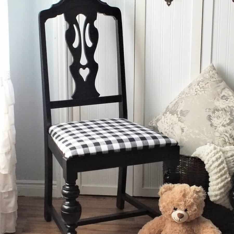 Vintage black-painted chair with an intricate cutout backrest and a black-and-white gingham seat cushion, styled in a cozy corner with a teddy bear.