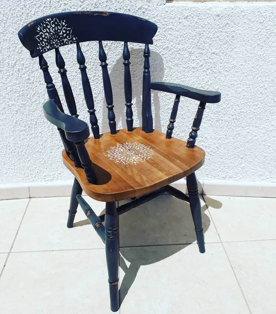 Vintage wooden armchair with navy blue spindles and a natural wood seat, featuring elegant white stencil detailing on the seat and backrest.