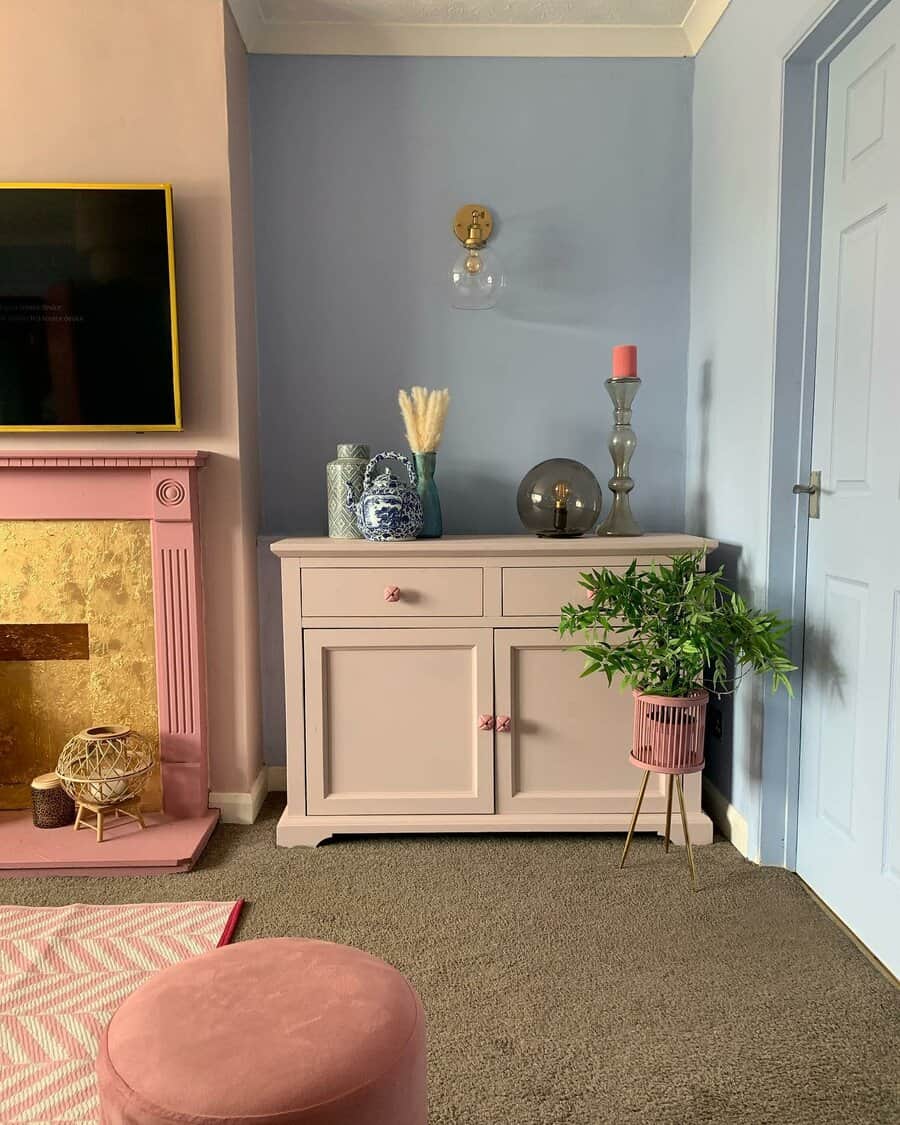 Pastel pink sideboard with floral knobs, styled with decorative vases, a candle, and a potted plant, set in a cozy, colorful living room.