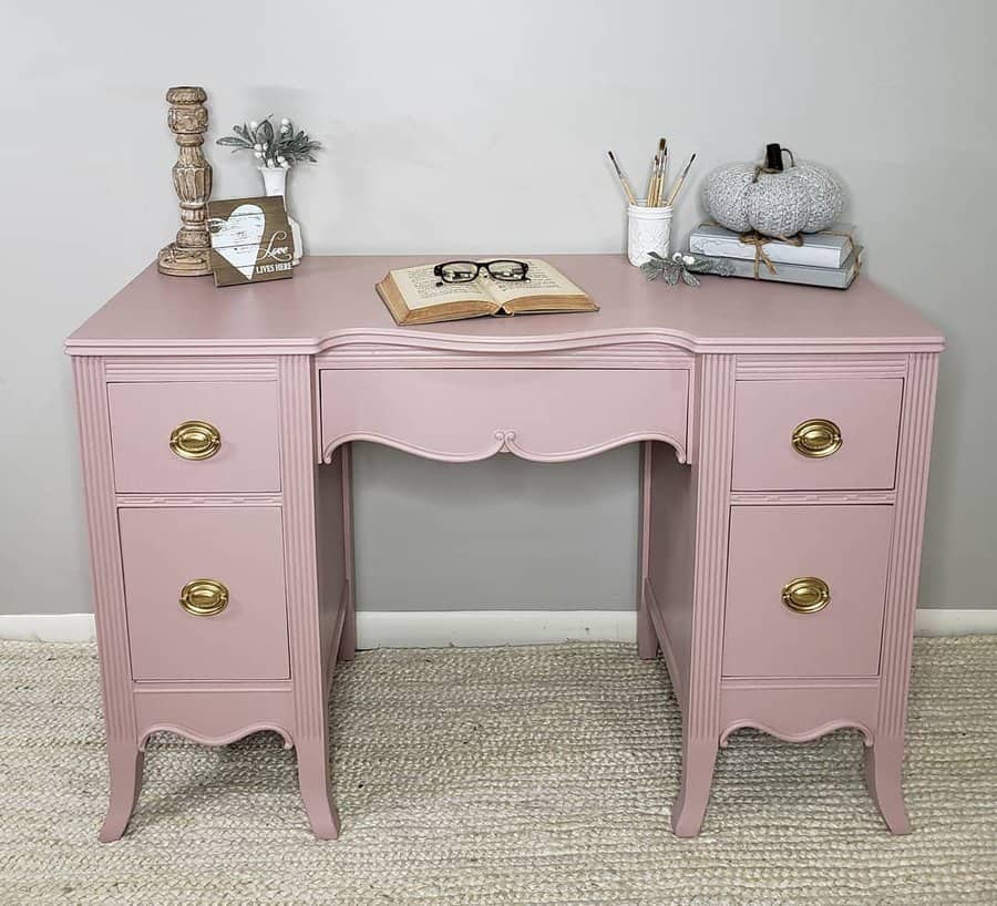 Vintage desk painted in soft blush pink with gold hardware, styled with an open book, rustic decor, and a cozy knitted pumpkin accent.