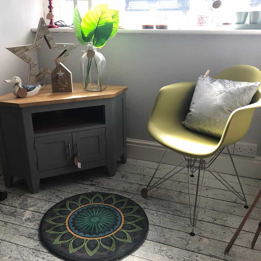 Cozy corner featuring a dark gray-painted cabinet with a wooden top, a modern green chair with a metallic base, and decorative accents.