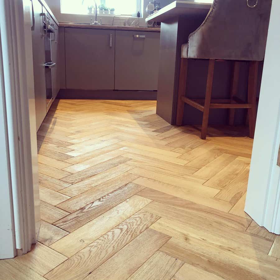 Kitchen with herringbone-patterned wooden floor, gray cabinets, and a brown cushioned barstool by an island