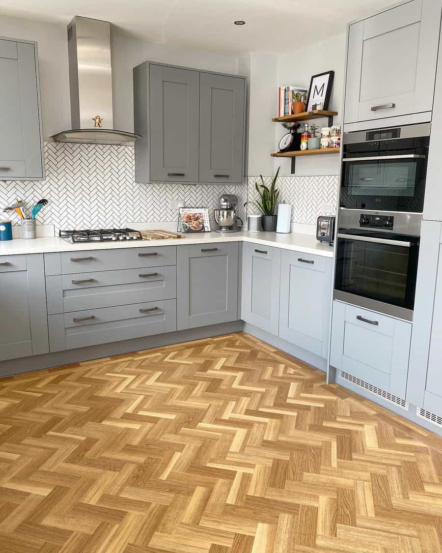 Modern kitchen with gray cabinets, herringbone wood floor, built-in oven, gas stove, and white herringbone-tiled backsplash