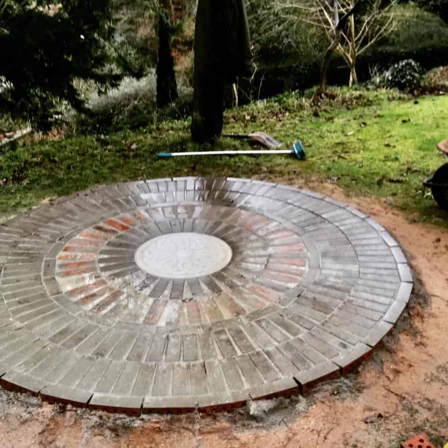 Circular brick patio with a central pattern, surrounded by grass