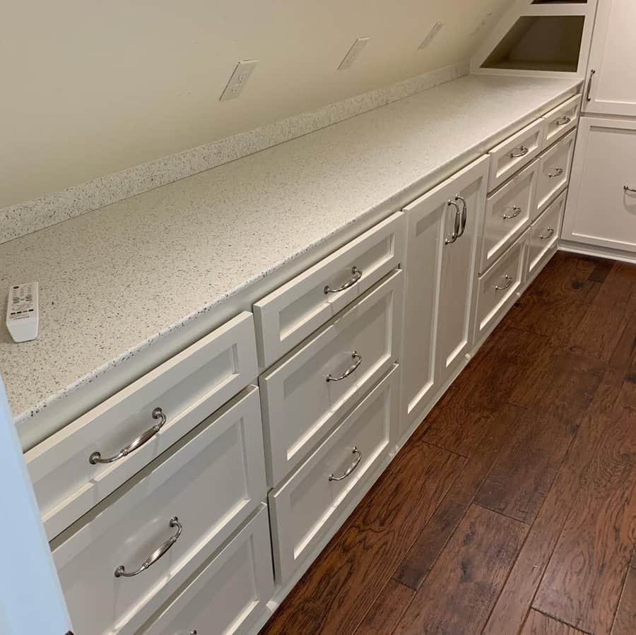 Custom-built white storage cabinets with drawers and a long countertop in an attic, maximizing space under a sloped ceiling.