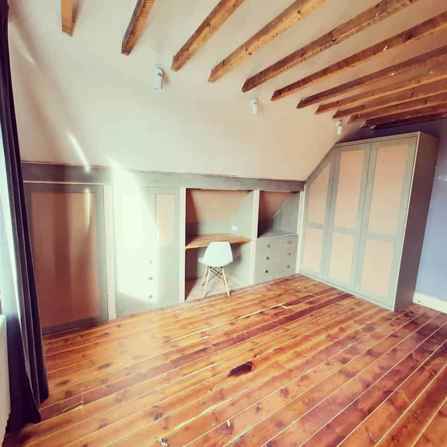 Attic room with built-in storage, a cozy desk nook, and exposed wooden beams, maximizing space with a stylish and functional design.