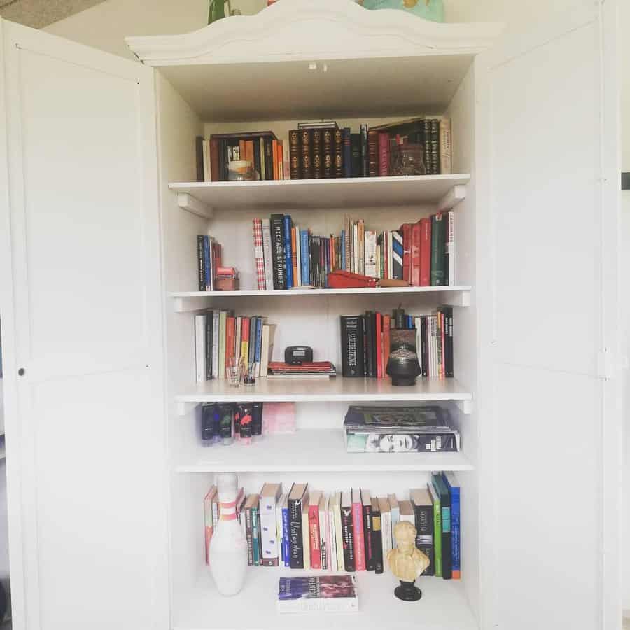 White armoire repurposed as a bookshelf, filled with books and decorative items, with open doors revealing neatly arranged shelves.