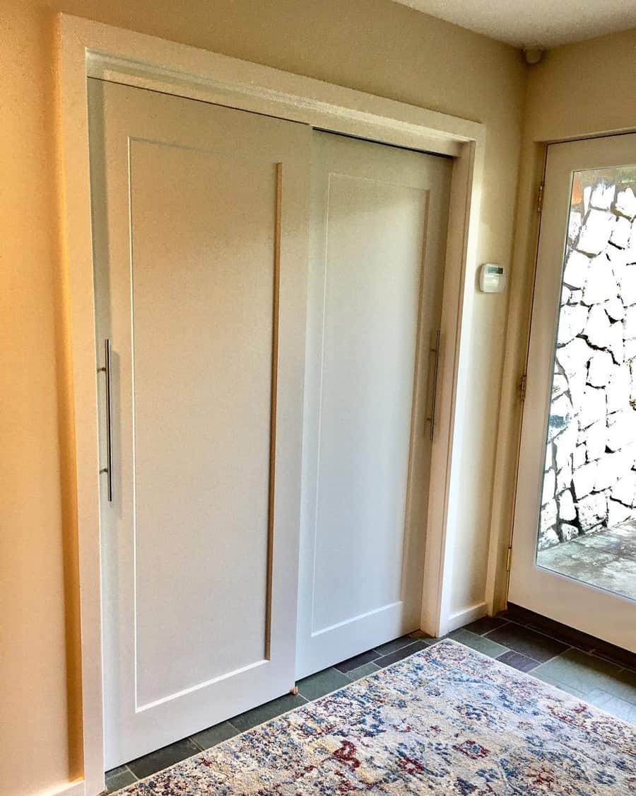 White sliding closet doors in a hallway, next to a glass door, with a colorful patterned rug on the floor