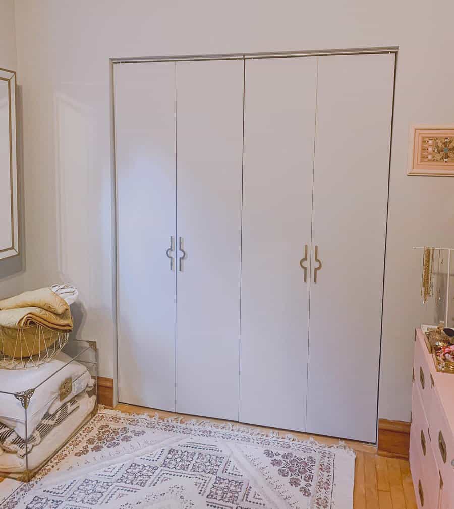 White closet doors in a room with light walls, a basket with blankets and a dresser nearby, and a patterned rug covering the floor