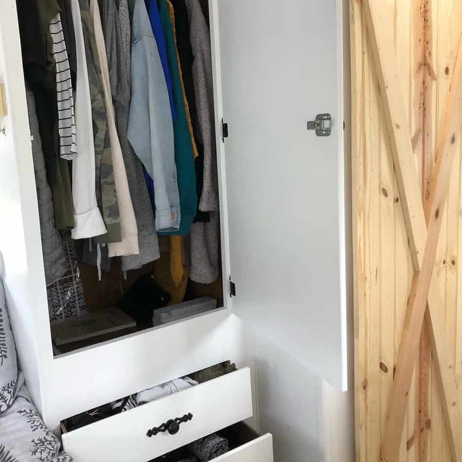 Compact RV closet with hanging clothes, two open drawers, and a white door with a latch, maximizing small space storage.