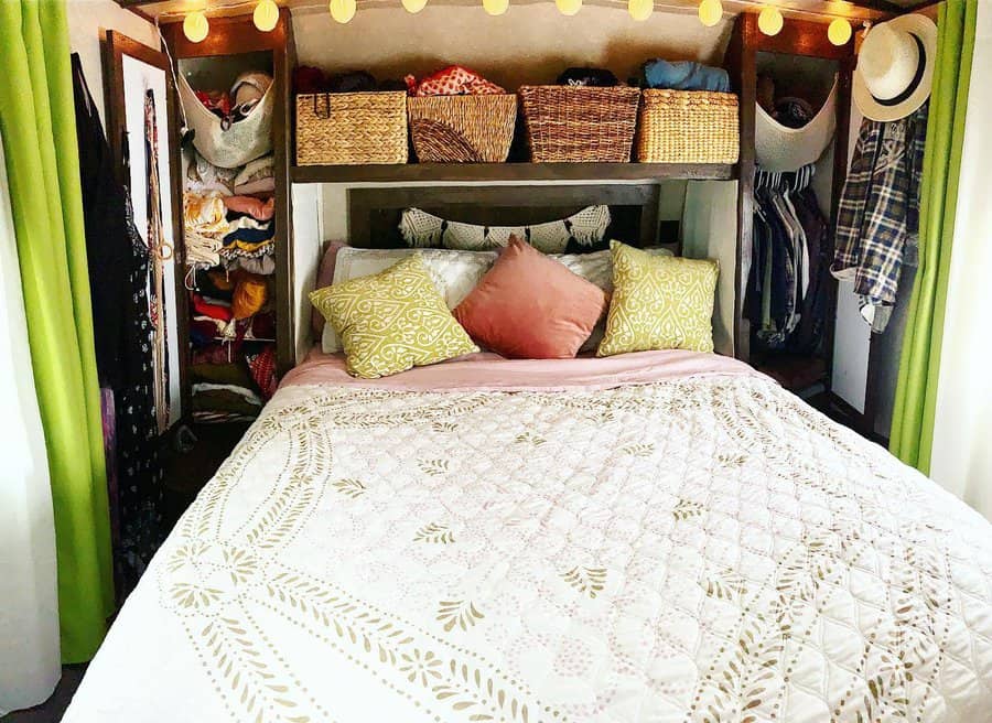 Cozy RV bedroom with overhead basket storage, side closets, hanging organizers, and warm lighting, blending function with boho charm.