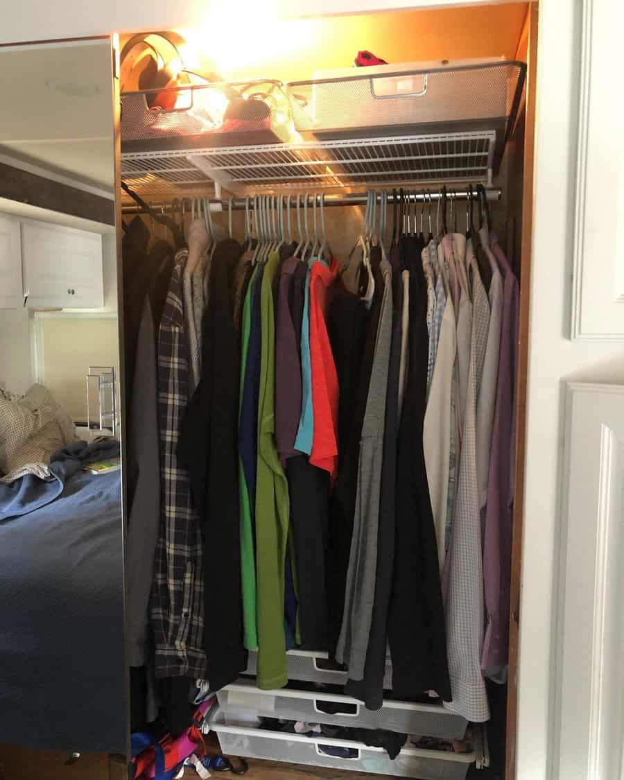 Well-organized RV closet with hanging clothes, a wire shelf for storage bins, and pull-out drawers, maximizing vertical space.