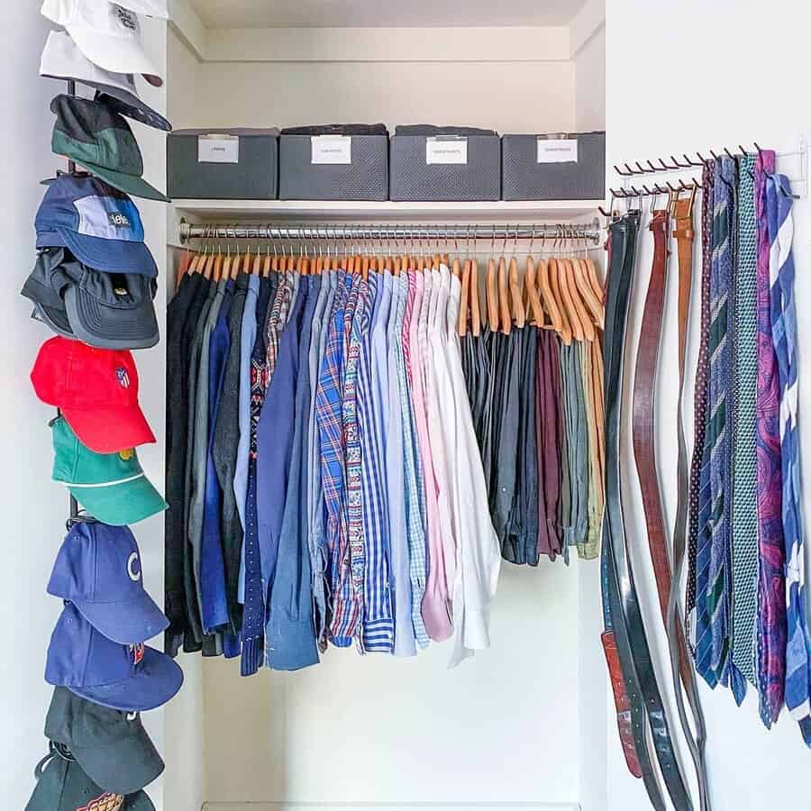 Closet with neatly hung shirts, belts, and ties; shelved boxes above and colorful caps organized on the left wall