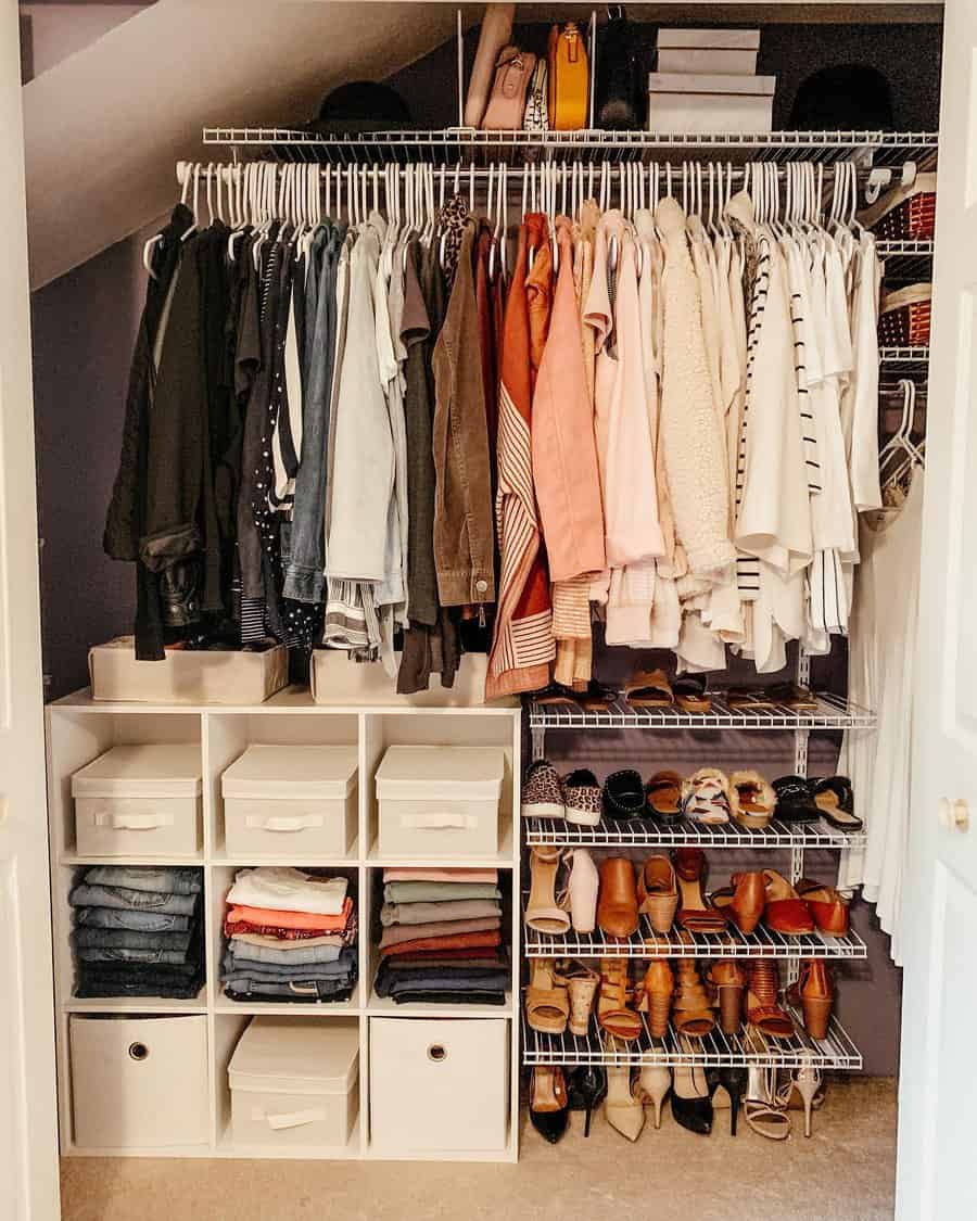 A neatly organized closet with color-coordinated clothes on hangers, shelves with folded jeans, shoes, and boxes on the floor and top shelf