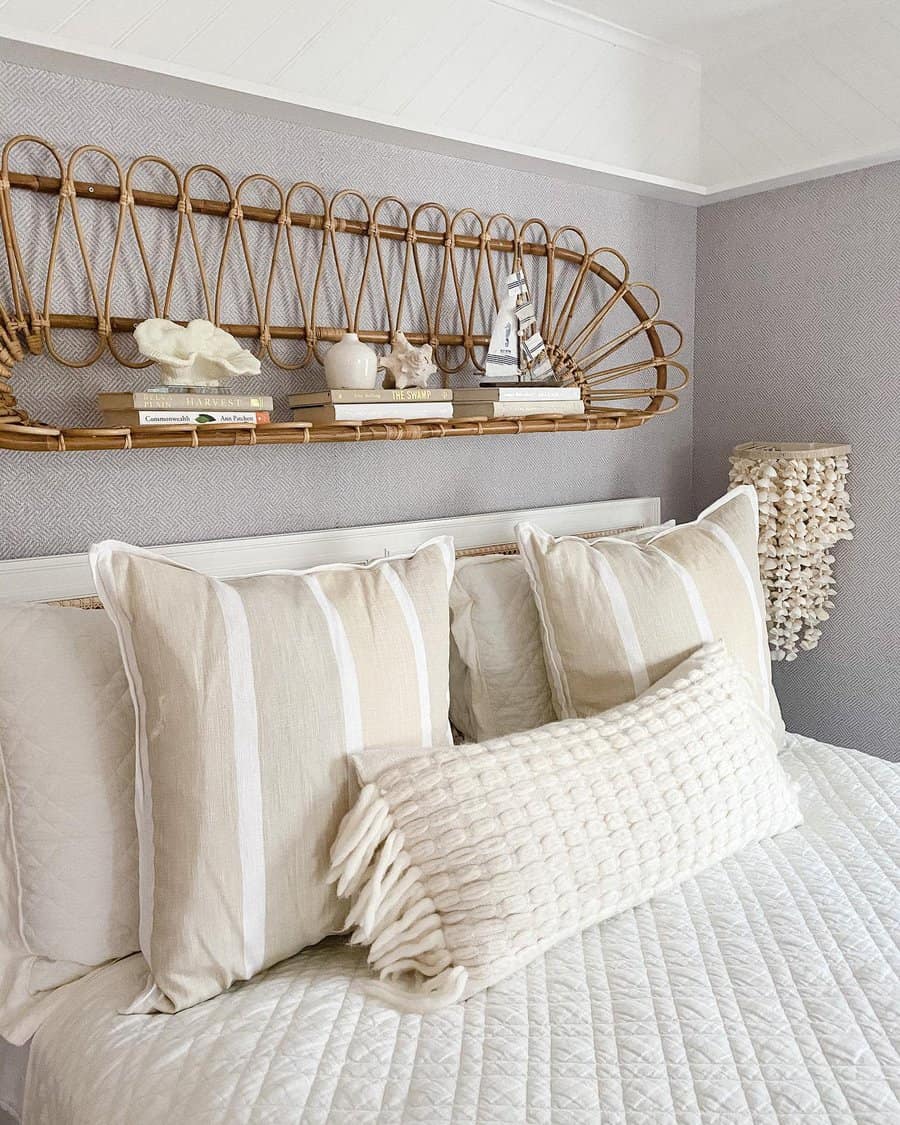 Bedroom with neutral tones, featuring a bed with striped pillows and a textured cushion. A decorative shelf with books and ornaments above.