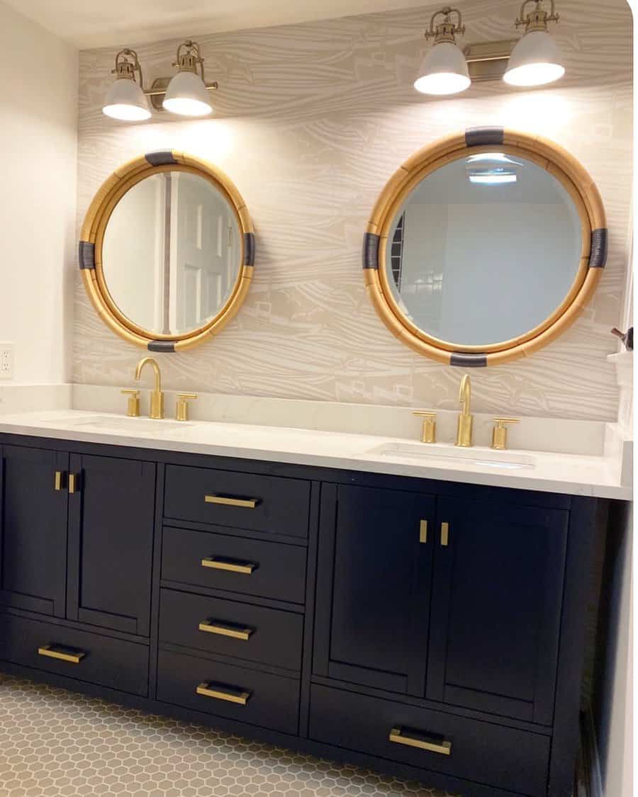 Bathroom with dual sinks, round mirrors, black vanity, gold faucets, and hexagonal floor tiles