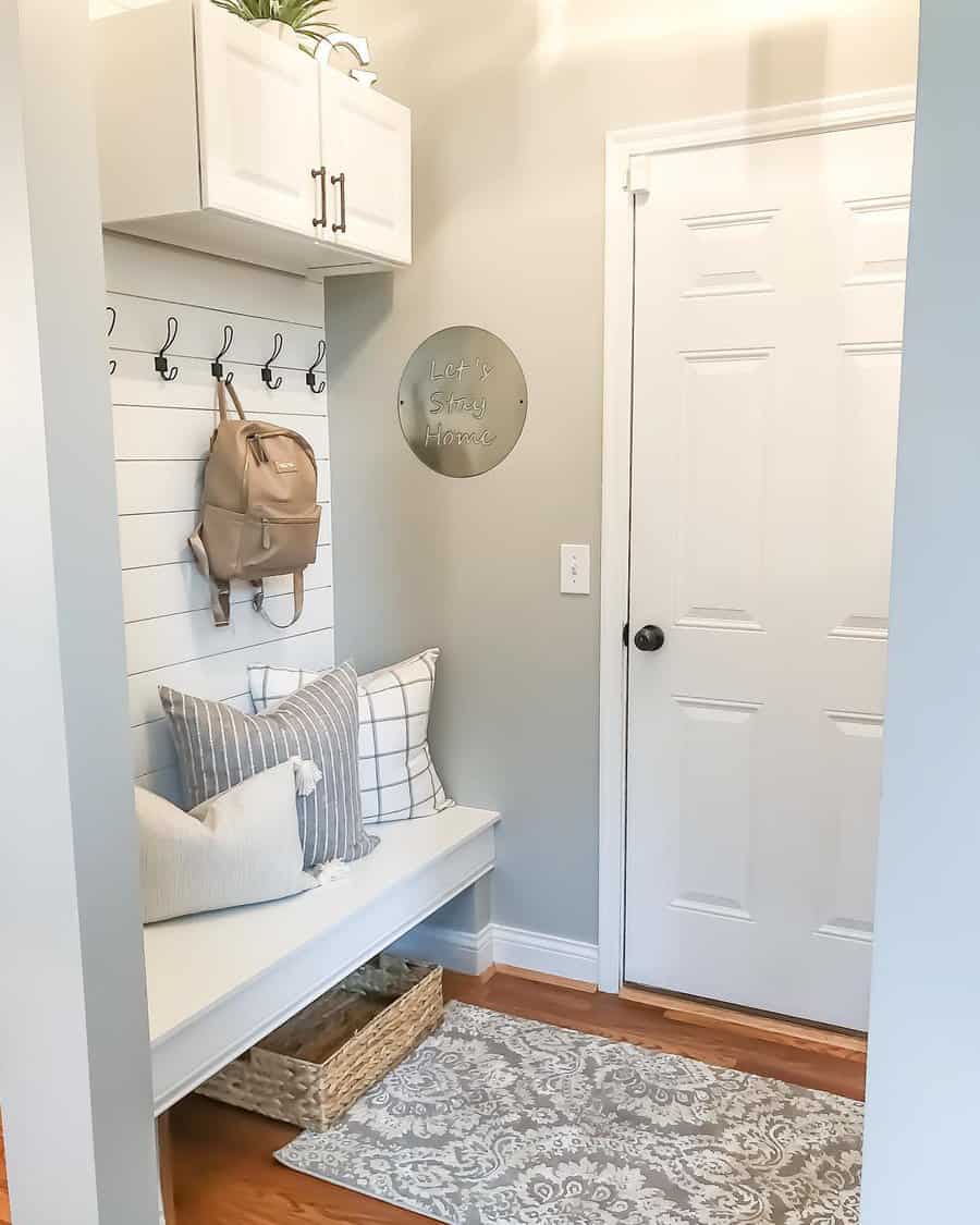 Bright and cozy entryway with a white shiplap wall, built-in bench, black hooks, soft pillows, and woven storage, creating a welcoming space