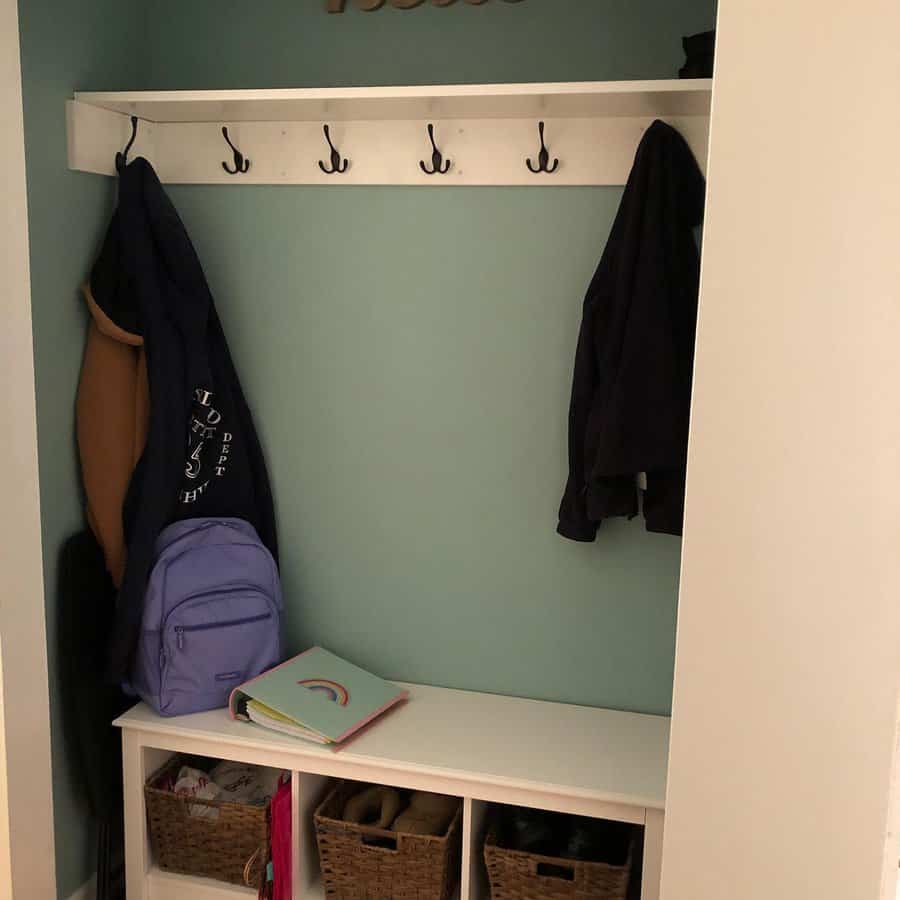 Compact entryway nook with a teal accent wall, white bench, black hooks, and woven baskets for organized storage and a cozy feel