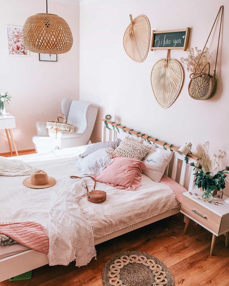 Cozy bedroom with a white bed, pink pillows, woven decor on the wall, and a white armchair; featuring warm tones and natural textures