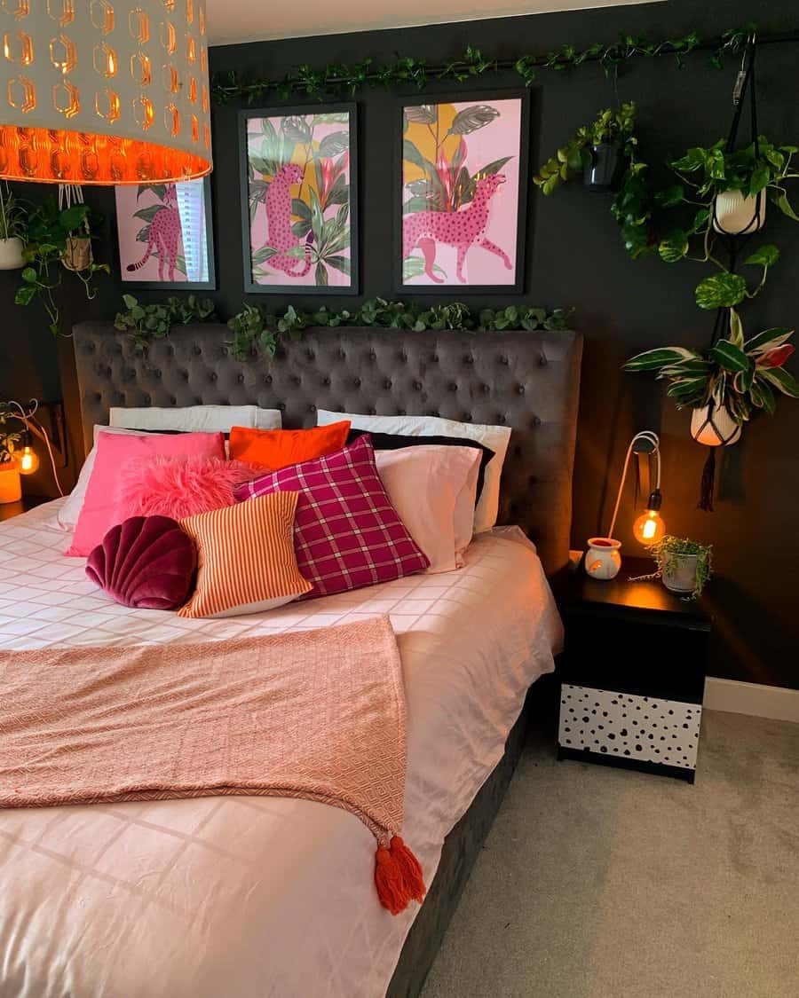 A cozy bedroom with a large bed, colorful pillows, pink and orange accents, leafy green plants, and vibrant wall art