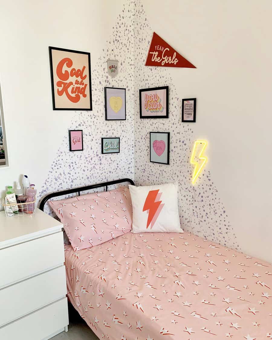 A monochrome bedroom with a pink bedspread and lightning bolt pillow, featuring wall art with positive quotes and a neon lightning sign