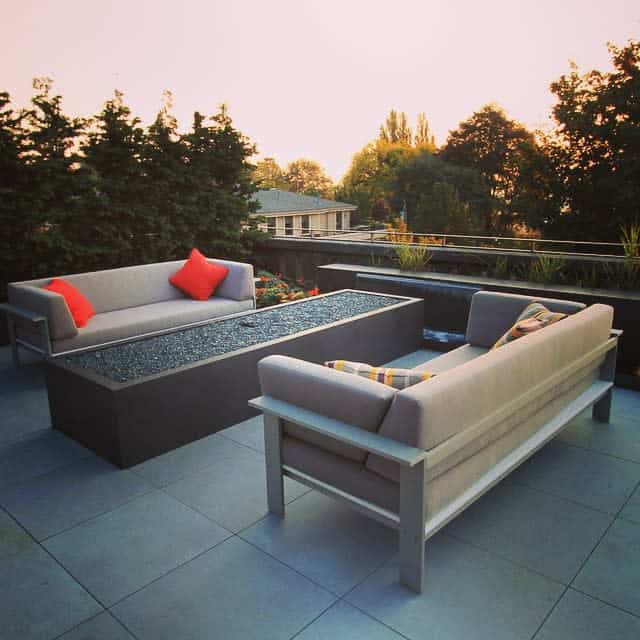 Modern rooftop patio with sleek concrete pavers, minimalist sofas, a linear fire pit, and vibrant accent pillows for a cozy yet stylish outdoor space