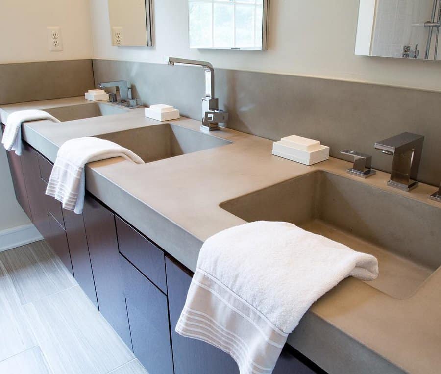 Contemporary bathroom with double integrated concrete sinks, matching backsplash, sleek faucets, and dark wood cabinetry.