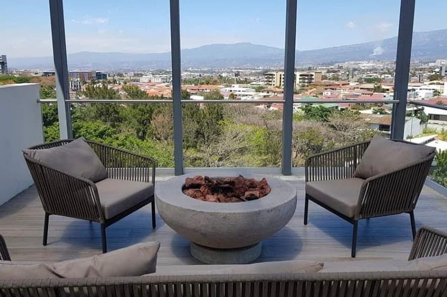 Balcony with two chairs and a round stone fire pit overlooking a cityscape and mountains