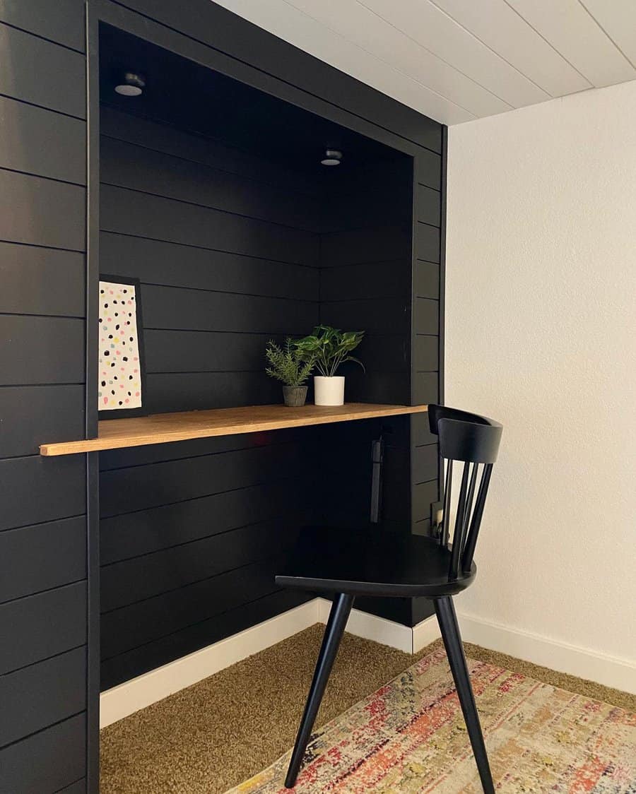 Minimalist home workspace with a black chair, wooden desk, plants, a polka dot notebook, and a colorful rug on the floor