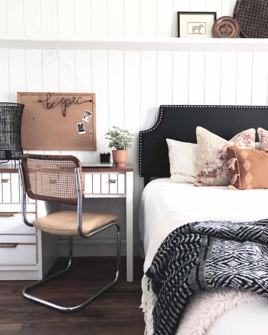 Cozy bedroom office with a white desk, rattan chair, and black studded headboard, blending rustic and modern elements for a warm workspace