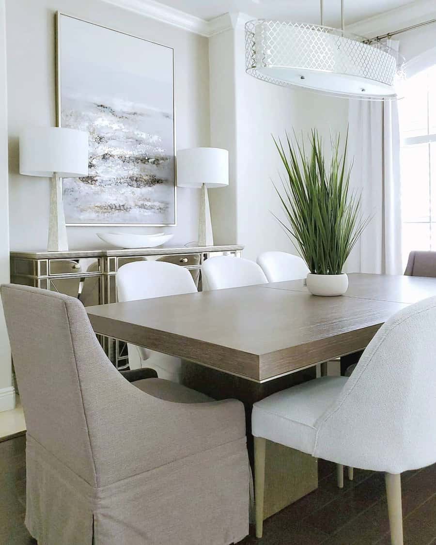 Modern dining room with a wooden table, various white and gray chairs, a plant centerpiece, lamps, and abstract wall art