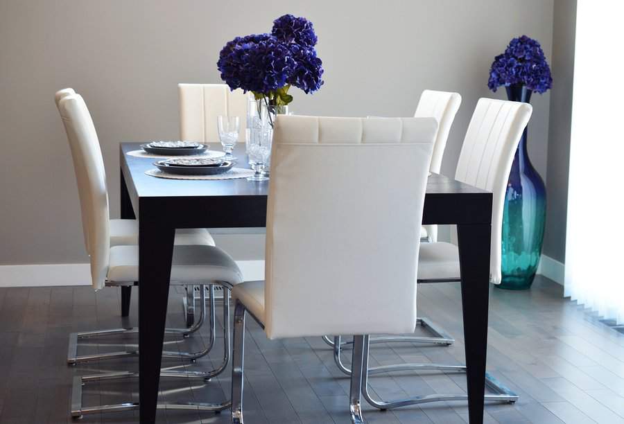 Modern dining room with a dark wooden table, white chairs, blue hydrangeas in vases, and a light gray wall