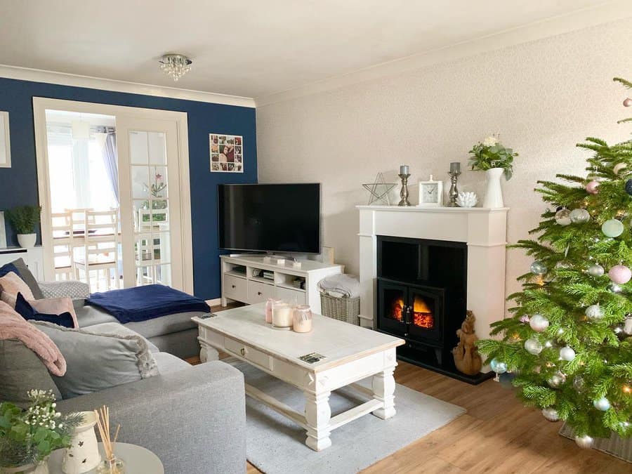 Cozy living room with a gray sofa, TV, white coffee table, fireplace, and decorated Christmas tree near the wall