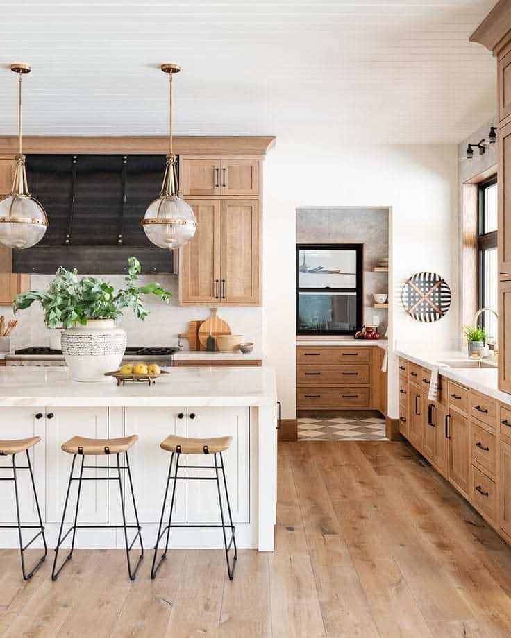 A modern kitchen with wooden cabinets, white island, and hanging pendant lights