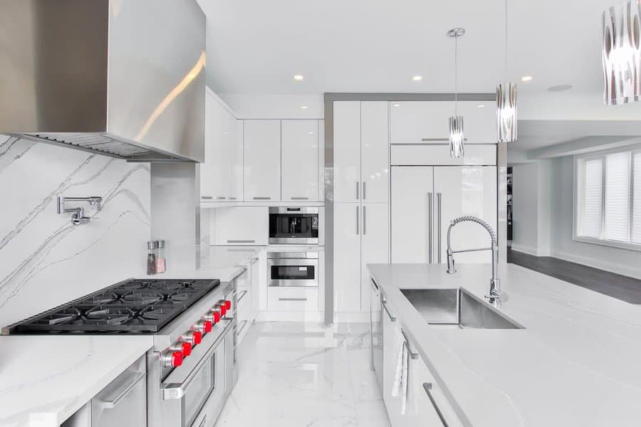 Modern white kitchen with stainless appliances, large island, and marble countertops