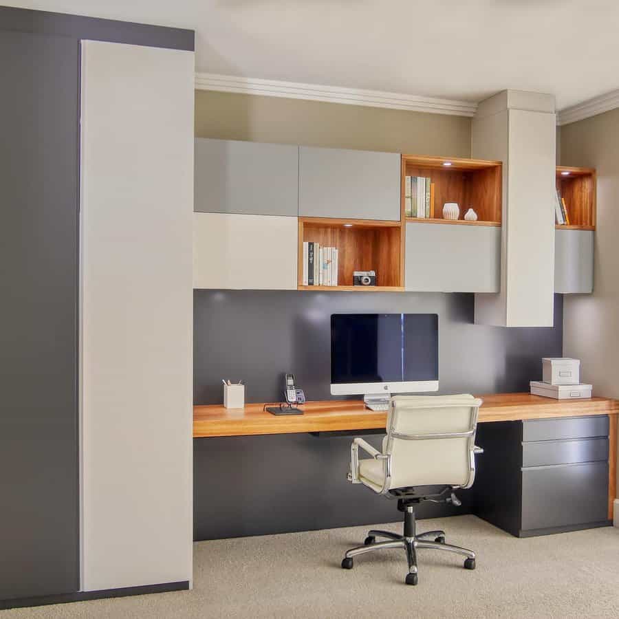 Modern home office with a large desk, computer, and white swivel chair; shelves with decor and neutral-toned cabinets above